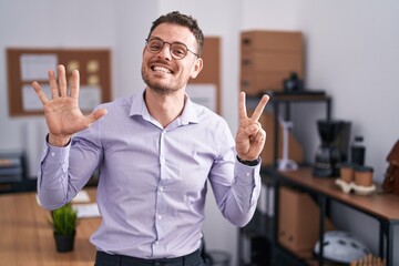 Young hispanic man at the office showing and pointing up with fingers number seven while smiling...