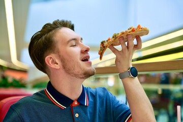 Portrait of handsome happy guy, young man is eating biting slice of tasty pizza, Italian food at...