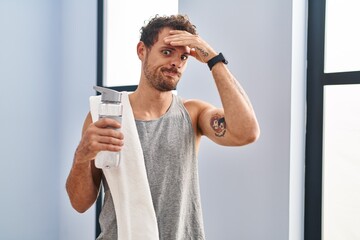 Young hispanic man wearing sportswear drinking water worried and stressed about a problem with hand on forehead, nervous and anxious for crisis