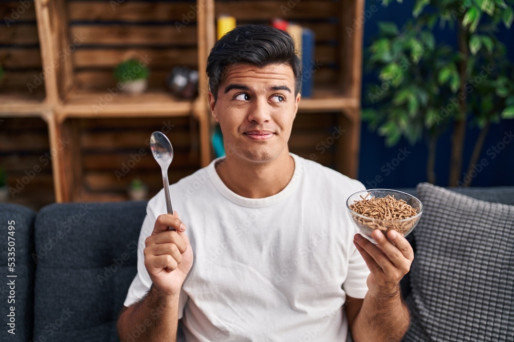 Sticker Hispanic man eating healthy whole grain cereals with spoon smiling looking to the side and staring away thinking.