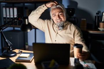 Middle age man with grey hair working at the office at night smiling confident touching hair with...