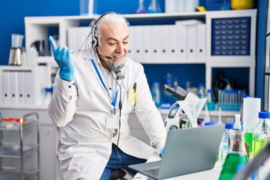 Middle Age Man With Grey Hair Working At Scientist Laboratory Doing Video Call Smiling Happy Pointing With Hand And Finger To The Side