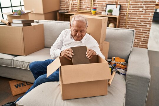 Senior man smiling confident unboxing package at new home