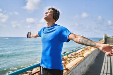 Young latin man breathing using headphones and smartphone at the beach.