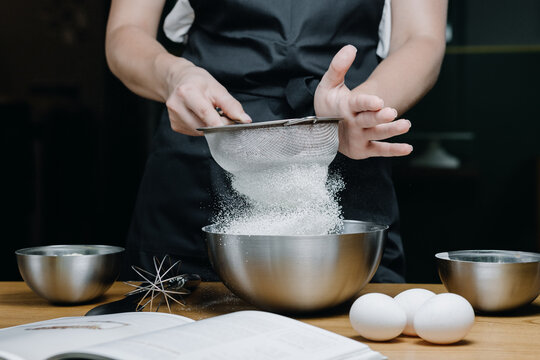 Cropped Image Of Female Pastry Chef Sifting Flour For Homemade Baking, Woman In Apron Holding Sieve Surrounded By Baking Ingredients.