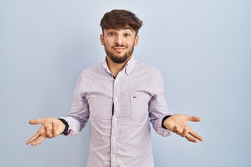 Arab man with beard standing over blue background clueless and confused with open arms, no idea concept.