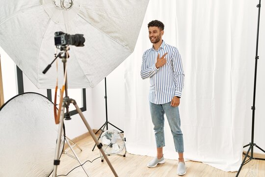 Arab young man posing as model at photography studio cheerful with a smile on face pointing with hand and finger up to the side with happy and natural expression