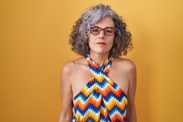 Middle age woman with grey hair standing over yellow background relaxed with serious expression on face. simple and natural looking at the camera.