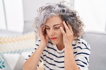 Middle age grey-haired woman suffering for headache sitting on sofa at home