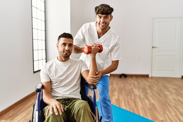Two hispanic men physiotherapist and patient sitting on wheelchair having rehab session using...