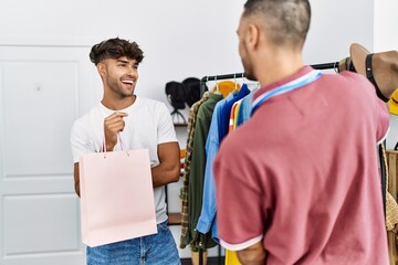 Young hispanic shopkeeper showing clothes to customer at clothing store.