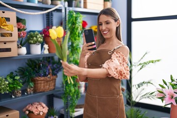 Young beautiful hispanic woman florist make photo to flower by smartphone at flower shop