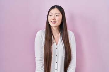 Fototapeta premium Chinese young woman standing over pink background looking away to side with smile on face, natural expression. laughing confident.