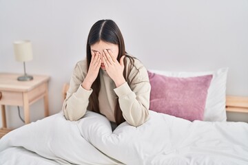 Chinese woman sitting on bed with serious expression at bedroom