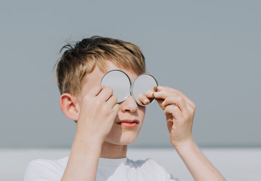 Preteen Boy Outdoors Holding Up Mirror Glasses To Eyes For Mental Health Awareness / Child Psychology