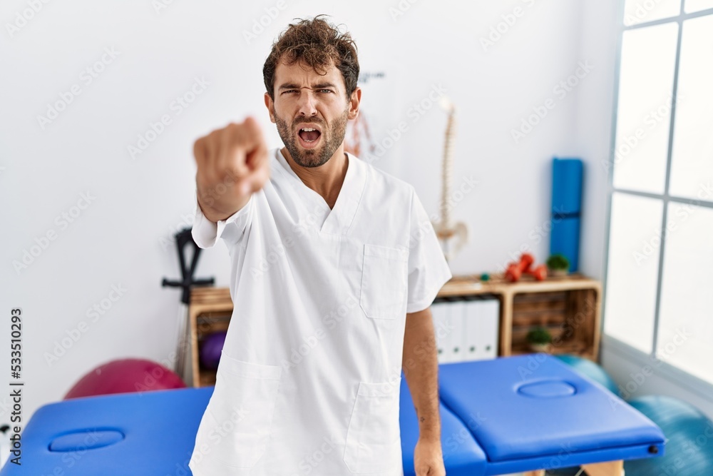 Canvas Prints Young handsome physiotherapist man working at pain recovery clinic pointing displeased and frustrated to the camera, angry and furious with you