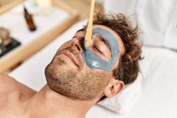 Young hispanic man having facial mask treatment at beauty center