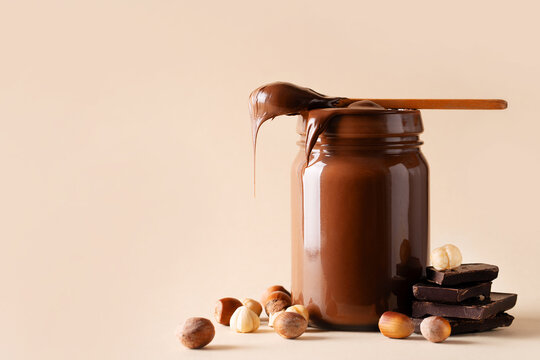 Chocolate paste in jar with nuts on cut wooden board