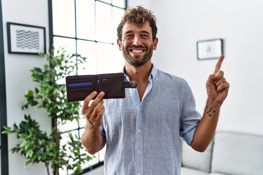 Young handsome man holding leather wallet smiling happy pointing with hand and finger to the side