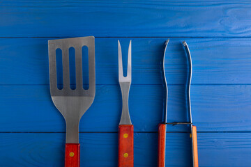 A set of used barbecue tools on a blue textured background.