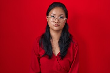 Asian young woman standing over red background relaxed with serious expression on face. simple and natural looking at the camera.