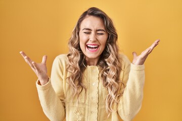 Young caucasian woman standing over yellow background celebrating mad and crazy for success with...