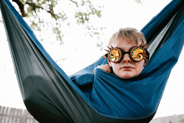 Preteen boy sits in a hammock wearing kaleidoscope glasses 