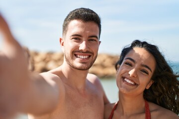 Obraz premium Young hispanic couple tourists wearing swimsuit make selfie by camera at seaside