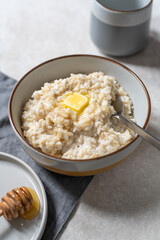 Unusual healthy delicious rice pudding made from brown rice and plant based milk served with butter and honey in grey bowl