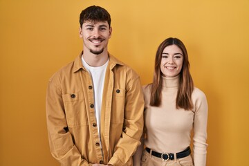 Young hispanic couple standing over yellow background with a happy and cool smile on face. lucky person.