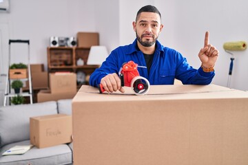 Hispanic man working on moving holding packing tape surprised with an idea or question pointing...