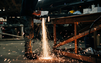 Industrial welder at work cutting steel metal with an angle grinder creating sparks in his workshop