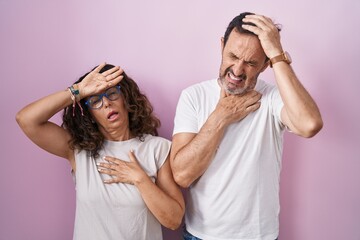 Middle age hispanic couple together over pink background touching forehead for illness and fever, flu and cold, virus sick