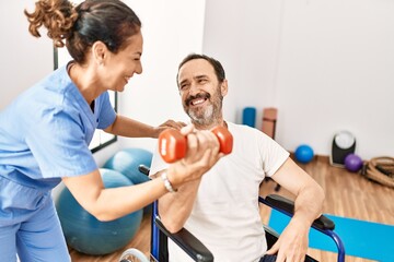 Obraz premium Middle age man and woman having rehab session using dumbbell sitting on wheelchair at physiotherapy clinic