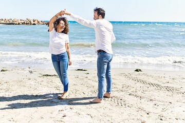Middle age hispanic couple smiling happy dancing at the beach.
