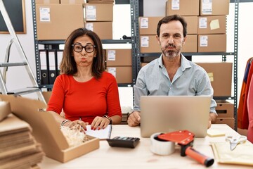 Middle age couple working at small business ecommerce puffing cheeks with funny face. mouth...
