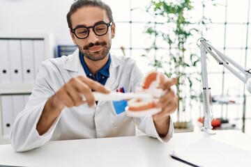 Handsome hispanic man working as dentist showing how to brush teeth at dentist clinic