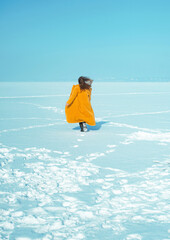 Young running woman in yellow coat walking on snowy ice. 