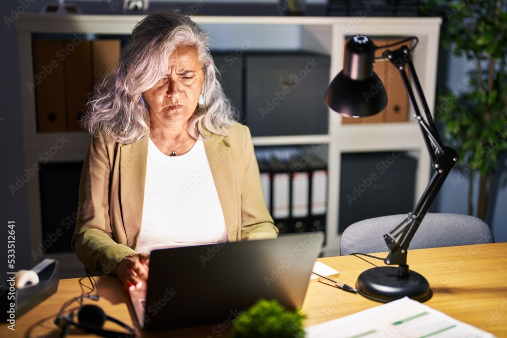 Sticker middle age woman with grey hair working using computer laptop late at night skeptic and nervous, fro