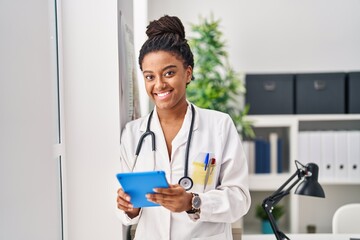 African american woman wearing doctor uniform using touchpad working at clinic