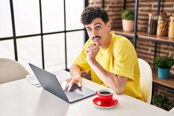 Young caucasian man using laptop drinking coffee at home