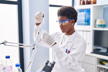 African american woman wearing scientist uniform measuring liquid at laboratory