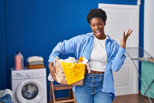 African american woman holding laundry basket celebrating victory with happy smile and winner expression with raised hands