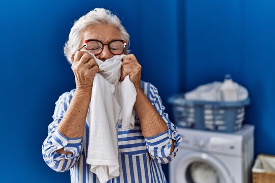 Senior Grey-haired Woman Smiling Confident Smelling Cleaning T Shirt At Laundry Room