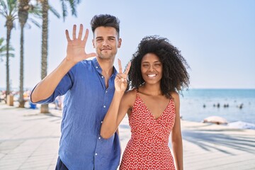 Young interracial couple outdoors on a sunny day showing and pointing up with fingers number seven...