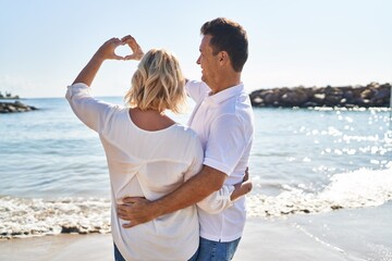 Middle age man and woman couple doing heart symbol with hands at seaside