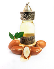 Argan oil in a oriental glass and metal bottle and argan nuts with green leaves isolated on white background.
