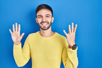 Naklejka premium Hispanic man standing over blue background showing and pointing up with fingers number nine while smiling confident and happy.