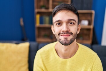 Obraz premium Young hispanic man smiling confident sitting on sofa at home