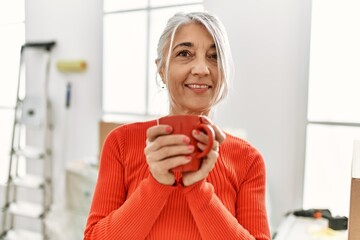 Middle age grey-haired woman smiling confident drinking coffee at new home